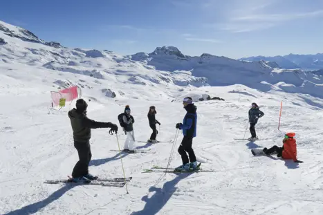 En grupp skidåkare står i backen i Cervinia, Italien, med de snötäckta Alperna i bakgrunden och njuter av en paus mellan åkningarna.
