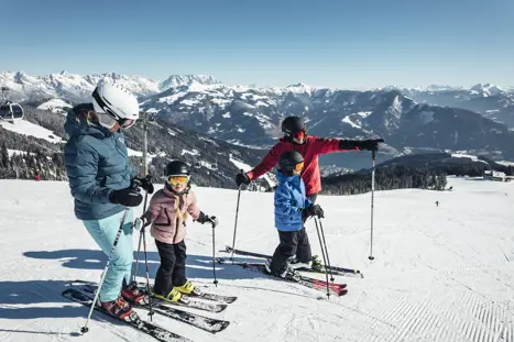 En familj med 2 vuxna och 2 barn planerar nästa åk nerför skidbacken i Zell Am See och njuter av utsikten av berg och snötäckta toppar.