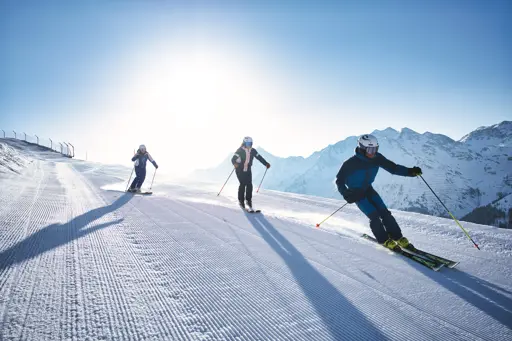 Tre skidåkare åker nerför en nypistad backe i St. Anton, Alperna, en populär skidort i Österrike