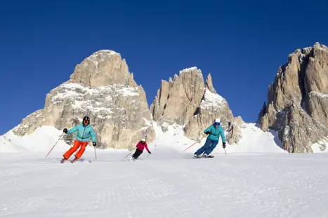En av många soliga dagar och tre skidåkare som åker skidor i takt med varandra i Canazei och får uppleva de imponerande och enorma Dolomitbergen.