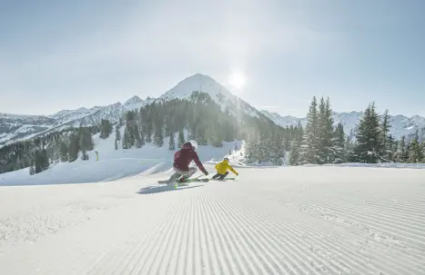 Två skidåkare åker nerför en välpreparerad pist i Schladming, i skidområdet där 230 km pist i Hochwurzen, Hauser Kaibling, Planai och Reiteralm ingår.