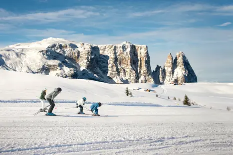 En familj som tar sats i skidbacken i Canazei, med Dolomiterna och deras majestätiska berg i bakgrunden, nära Sella Ronda-massivet, där den berömda Sella Ronda-turen går.