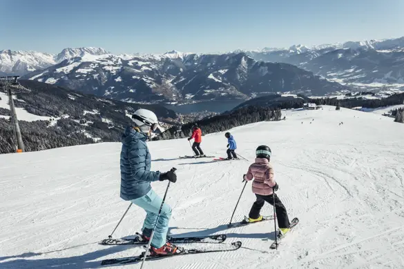 En familj åker skidor i skidområdet Zell am See-Kaprun, tar breda svängar på de snötäckta pisterna i soligt vinterväder.